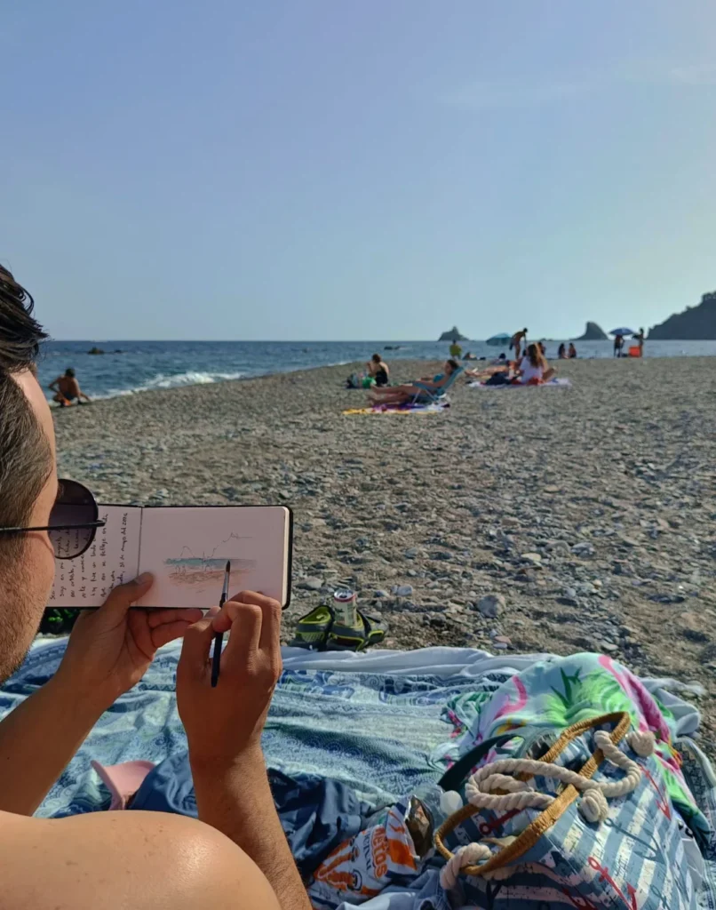 Yohan Pixone pintando una acuarela al aire libre en la playa de Almuñécar durante una práctica de cuaderno de obra.
