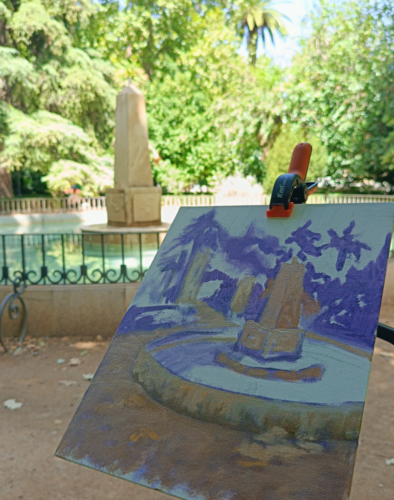 Caballete y materiales de pintura de Yohan Pixone bajo los árboles, junto a una fuente del centro de Granada.